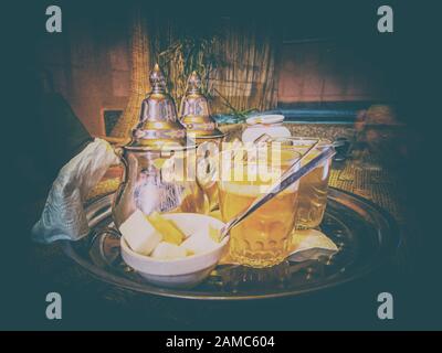 Vintage-Hintergrund mit frischem Minztee in typischen Tee-Metalltöpfen und -Gläsern in einem Restaurant in Marrakesch, Marokko. Es handelt sich um einen typischen Berbertee, der auch genannt wird Stockfoto