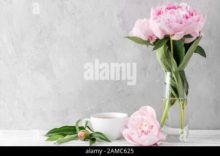 Festlicher Blumenstrauß mit pinkfarbenen Ponyblüten und Kaffeetasse auf weißem Tisch mit Kopierraum. Stillleben. Damen- oder Hochzeitshintergrund Stockfoto
