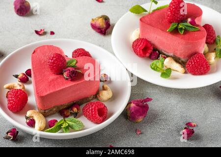 Valentins-Dessert. Herzförmige vegane rote Kuchen mit Himbeeren, getrockneten Rosenblüten und Minze. Gesunde köstliche Speisen. Nahaufnahme. Liebeskonzept Stockfoto