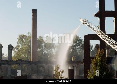 Eine alte historische Textilfabrik in wurde durch Brandstiftung zerstört. Die Feuerwehr löscht weiterhin Brände mit Wasser über ihre Lastwagen. Stockfoto