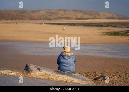 Eine Einzelfigur, die auf dem Schlupf sitzt, der nach Newton Beach bei Porthcawl, Südwales führt Stockfoto