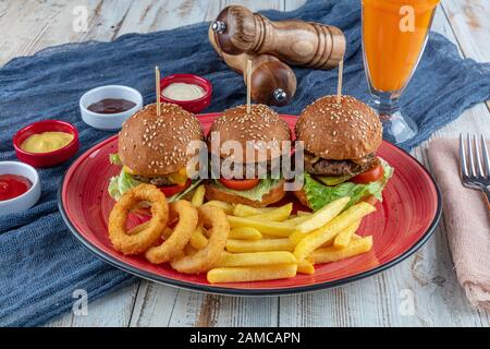 Drei Mini-Hamburger. Hausgemachte köstliche drei Mini-Burger mit Salat, Sauce und Zwiebelringen und pommes frites. Hausgemachte Mini-Burger-Schieberegler. Stockfoto