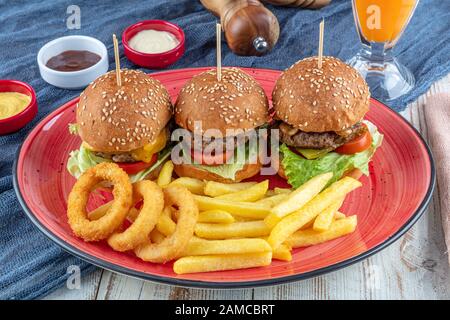 Drei Mini-Hamburger. Hausgemachte köstliche drei Mini-Burger mit Salat, Sauce und Zwiebelringen und pommes frites. Hausgemachte Mini-Burger-Schieberegler. Stockfoto