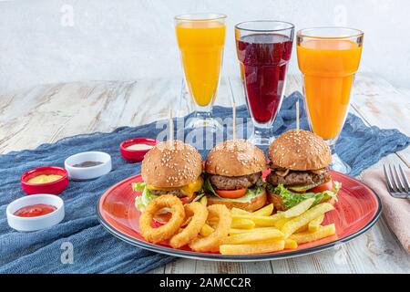 Drei Mini-Hamburger. Hausgemachte köstliche drei Mini-Burger mit Salat, Sauce und Zwiebelringen und pommes frites. Hausgemachte Mini-Burger-Schieberegler. Stockfoto