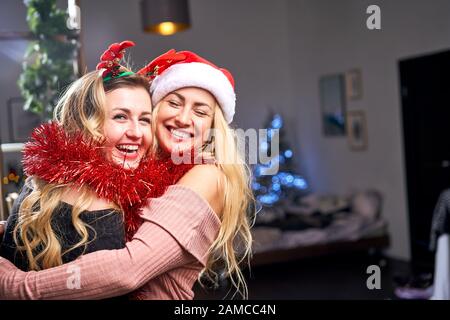 Zwei umarmende Frauen mit Tinsel während der Weihnachtsfeier in der Wohnung. Neujahr-Konzept Stockfoto