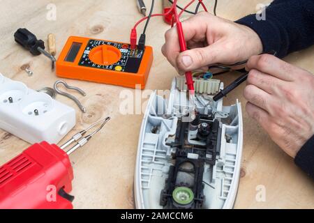 Die Hände des Elektrikers prüfen das defekte Bügeleisen mit dem Messgerät. Stockfoto