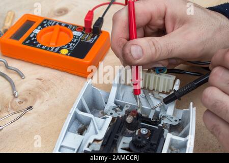 Die Hände des Elektrikers prüfen das defekte Bügeleisen mit dem Messgerät. Stockfoto