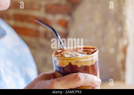 Nahansicht zur Hand halten ein Glas Eisschokolade, Kakao oder Kaffeemokka und verwischen den Hintergrund der rauhen Ziegelwand des Loft Vintage Style Cafés. Stockfoto