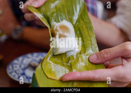 Gedämpftes Mehl mit Kokosnuss-Füllung, mit Bananenblatt umhüllt, Kanom Sai Sai, traditionelles thailändisches Dessert wird von zwei Händen umhüllt. Stockfoto