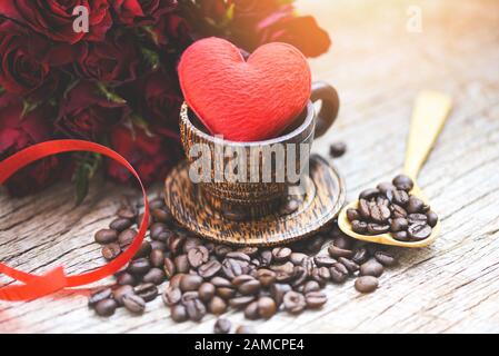 Herz in Holzkaffeetasse mit Kaffeebohnen romantischer Liebes-Valentinstag und roter Rosenblüte auf Holzhintergrund/Liebeskaffeekonzept Stockfoto