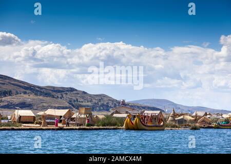 Schwimmende Inseln von Uros am Titicacasee in Peru, Südamerika - 2019-12-01. Auf der Insel sind ein Mann und zwei Frauen neben einem Touristenboot Stockfoto