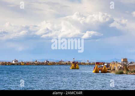 Schwimmende Inseln von Uros, Titicacasee, Peru, Südamerika - 2019-12-01. Blick auf die Insel, ein Boot vom Schilf, blauer Himmel in den Wolken. Stockfoto