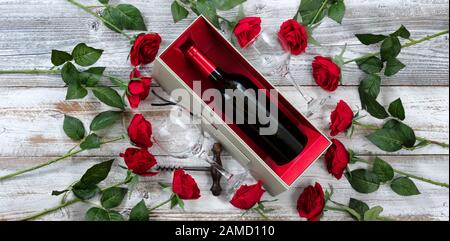Fröhliche Valentinstag mit roten Rosen und einer Flasche Wein auf weißem rustikalem Holzhintergrund Stockfoto