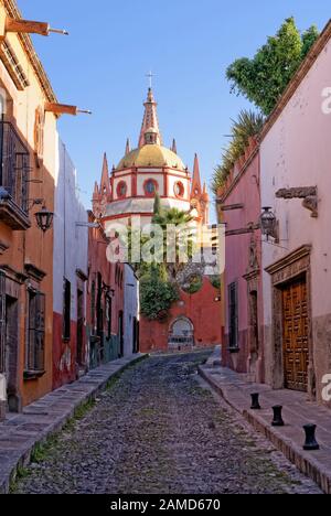 Blick auf die Straße Aldama Street mit Kopfsteinpflaster mit Kuppel und Kirchturm der Pfarrkirche La Parroquia in Back, San Miguel de Allende, Mexiko Stockfoto