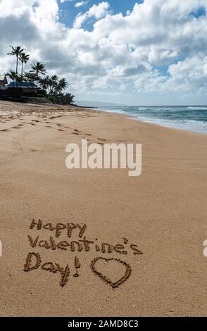 Fröhlicher Valentinstag mit einem Herz, das im Sand am Strand gezogen ist Stockfoto