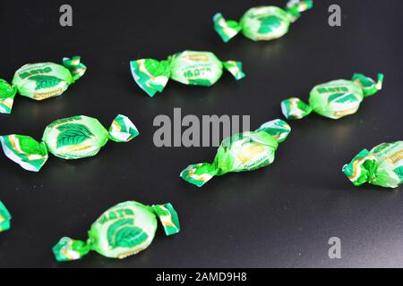 Schöne Minzwürste in der Verpackung, Minze schön auf der Oberfläche gelegt. Leckere grüne Süßigkeiten, Lollipops liegen auf einem schwarzen Kunststoffrücken. Stockfoto