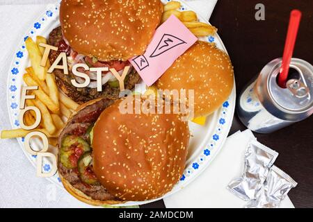 Saftige Burger und Pommes frites auf einem Papierteller mit Worten LECKERES ESSEN auf Burgern. Stockfoto