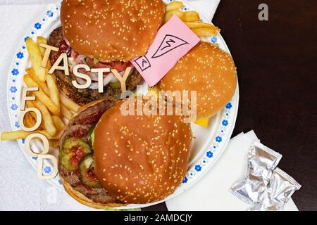 Saftige Burger und Pommes frites auf einem Papierteller mit Worten LECKERES ESSEN auf Burgern. Stockfoto