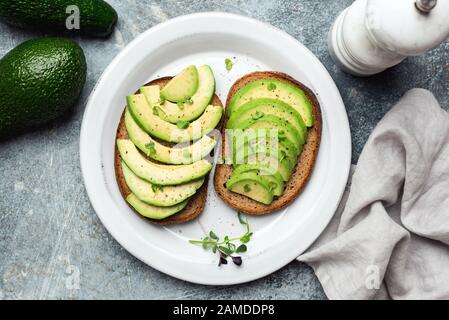 Avocado-Scheiben auf Roggenbrot garniert mit Mikrogrüns auf einem Teller, Draufsicht. Veganes, vegetarisches Avocado-Sandwich Stockfoto