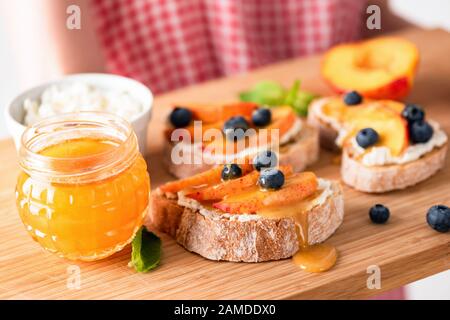 Süße Bruschetta mit Ricotta, Pfirsich und Honig auf einem Holzteller Gesunder Imbiss, Frühstück, sommerliches Picknickangebot Stockfoto