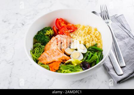 Gesundes Essen, Keto Food Konzept. Fischsalatschüssel auf marmorem Tischhintergrund. Salat mit Lachs, Couscous, Gemüse, Wachteleiern. Nahaufnahme Stockfoto