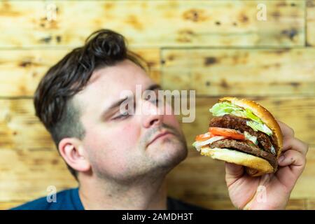 Gutaussehender junger Mann, der seinen Burger genießen wird. Fast Food Goodies. Stockfoto