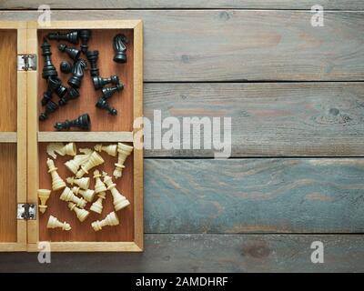 Schwarze und weiße Schachfiguren in einem Feld mit einem hölzernen Hintergrund Stockfoto