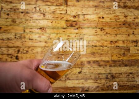 Mans-Hand, die Glas Bier hält. Holzhintergrund. Stockfoto