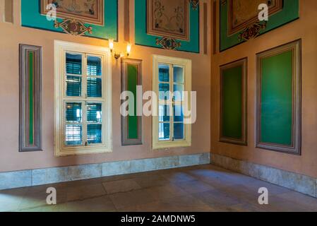 Ecke orangefarbene Wand mit zwei Holzfenstern mit grünen Fensterläden, schönen, eleganten, rechteckigen grünen Rahmen mit verzierten Rahmen und weißem gefliestem Marmorboden Stockfoto