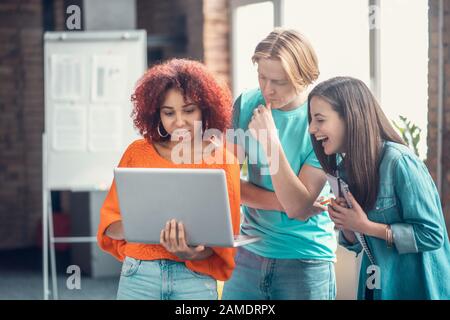 Geschweifte mulatto Studenten, die während des Studiums in der Nähe von Freunden einen Laptop halten Stockfoto