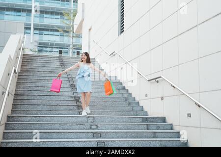 Freundliche asiatische Frau gehen Treppen mit bunten Shop Pakete. Shopping und Mode Konzept Stockfoto