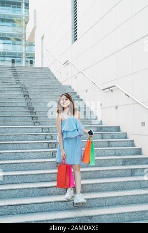 Junge asiatische lächelnd, Frau genießt beim gehen der Treppe das Einkaufen mit einer bunten Tasche. Stockfoto