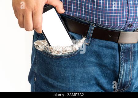 Mann legt ein Smartphone mit leerem Bildschirm in seine Tasche, die mit Aluminiumfolie bedeckt ist Stockfoto