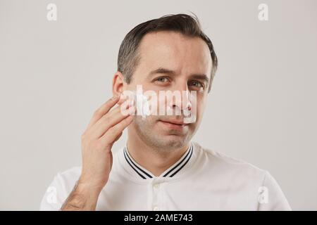Kopf und Schultern Portrait des Mannes mittleren Alters, der sich während der morgendlichen Routine auf Rasiercreme setzt, die vor weißem Hintergrund steht Stockfoto