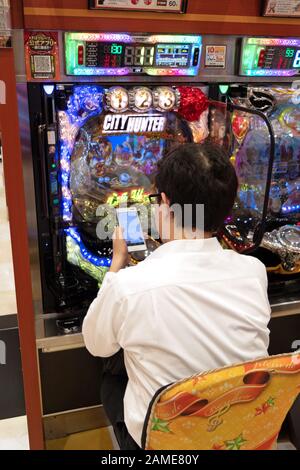 Japanischer Mann in Tokio, Japan, Asien mit Smartphone und spielen Pachinko, Lotterie, Arcade-Spiel, Videospiel, Videospiel, Glücksspiel am Spielautomaten in Asien Stockfoto