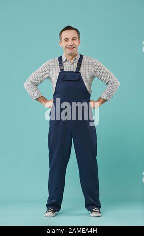 Porträt eines lächelnden Mittelalter-Mannes, der Arbeiteruniform trägt, fröhlich posiert, während er vor blauem Hintergrund steht Stockfoto