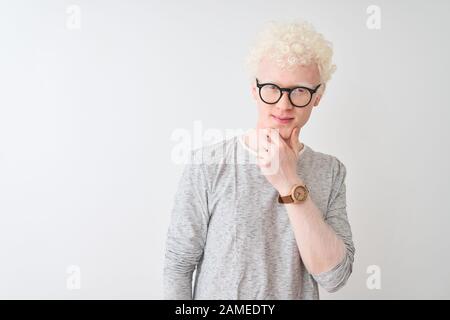 Junger albino blonder Mann mit gestreiftem T-Shirt und Brille über isoliertem weißem Hintergrund, der mit einem Lächeln und gekreuzten Armen zuversichtlich auf die Kamera blickt Stockfoto