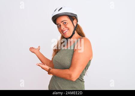 Ältere Radfahrerin im mittleren Alter, die einen Sicherheitshelm über isoliertem Hintergrund Trägt Und Mit offener Hand zum Smiling Natural einlädt Stockfoto