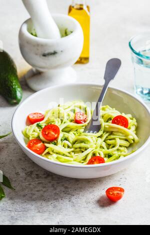 Zucchini Pasta mit Pesto, Avocado und Tomaten in einem weißen Teller. Rohes veganes Lebensmittelkonzept. Stockfoto