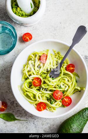 Zucchini Pasta mit Pesto, Avocado und Tomaten in einem weißen Teller. Rohes veganes Lebensmittelkonzept. Stockfoto