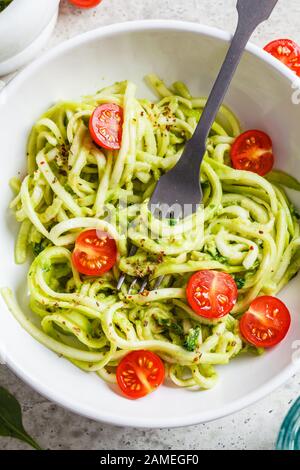 Zucchini Pasta mit Pesto, Avocado und Tomaten in einem weißen Teller. Rohes veganes Lebensmittelkonzept. Stockfoto