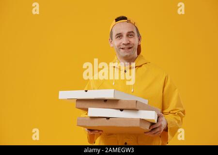 Taille hoch Portrait des erwachsenen Lieferers Mann mit Pizzabäckchen und fröhlichem Lächeln auf der Kamera vor gelbem Hintergrund, Kopierraum Stockfoto