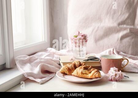 Frühlingsszene im Stillleben. Tasse Kaffee, Croissant Gebäck, alte Bücher und Scheren, feminines Foto im Vintage-Stil. Blumenapposition mit rosafarbenem Sakura, Stockfoto