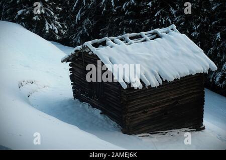 Eine fesselnde Szene mit einer alten Holzscheune, tief verwittert und rustikal, eingebettet in einen ruhigen, verschneiten Wald. Stockfoto