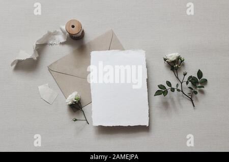 Moody Wedding stylte Komposition. Feminine Desktop-Mockup-Szene mit weißen Rosenblüten und Blättern, Seidenband, handwerksarmer Umhüllung und leerem Grußwagen Stockfoto