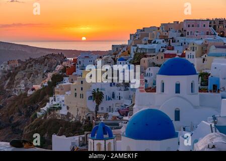 Blaue Kuppelkirchen und traditionelle weiße Häuser mit Blick auf die ägeische See und warmem Licht bei Sonnenuntergang in Oia, Santorini, Griechenland Stockfoto