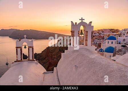 Blaue Kuppelkirchen und der Kirchturm mit Blick auf die ägeische See mit warmem Licht bei Sonnenuntergang in Oia, Santorini, Griechenland Stockfoto