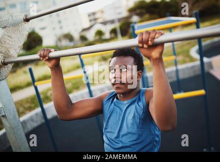 Portrait des entschlossenen, sportlichen jungen afroamerikanischen Mannes führt Pull-Ups-Übungen durch, um die Muskeln im Sportpark im Freien zu stärken Stockfoto