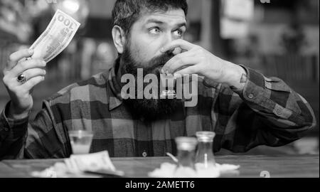 Mann mit betrunkenem Gesicht sitzt allein an der Theke. Hiphster hält Geld, Bargeld, um mehr Alkohol zu kaufen. Guy verbringen Sie Freizeit in der Bar mit einem Cocktail, unverschäumter Hintergrundfarbe. Getränkekonzept kaufen. Stockfoto