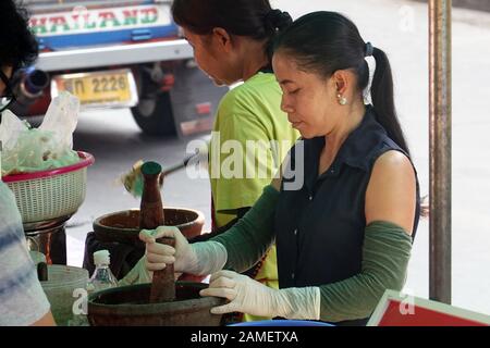 Bangkok, Thailand - 26. Dezember 2019: Frau des Straßenverkäufers, die einen großen Mörser und Pfirsich verwendet und Som tam, einen grünen Papaya-Salat, zubereitet. Stockfoto